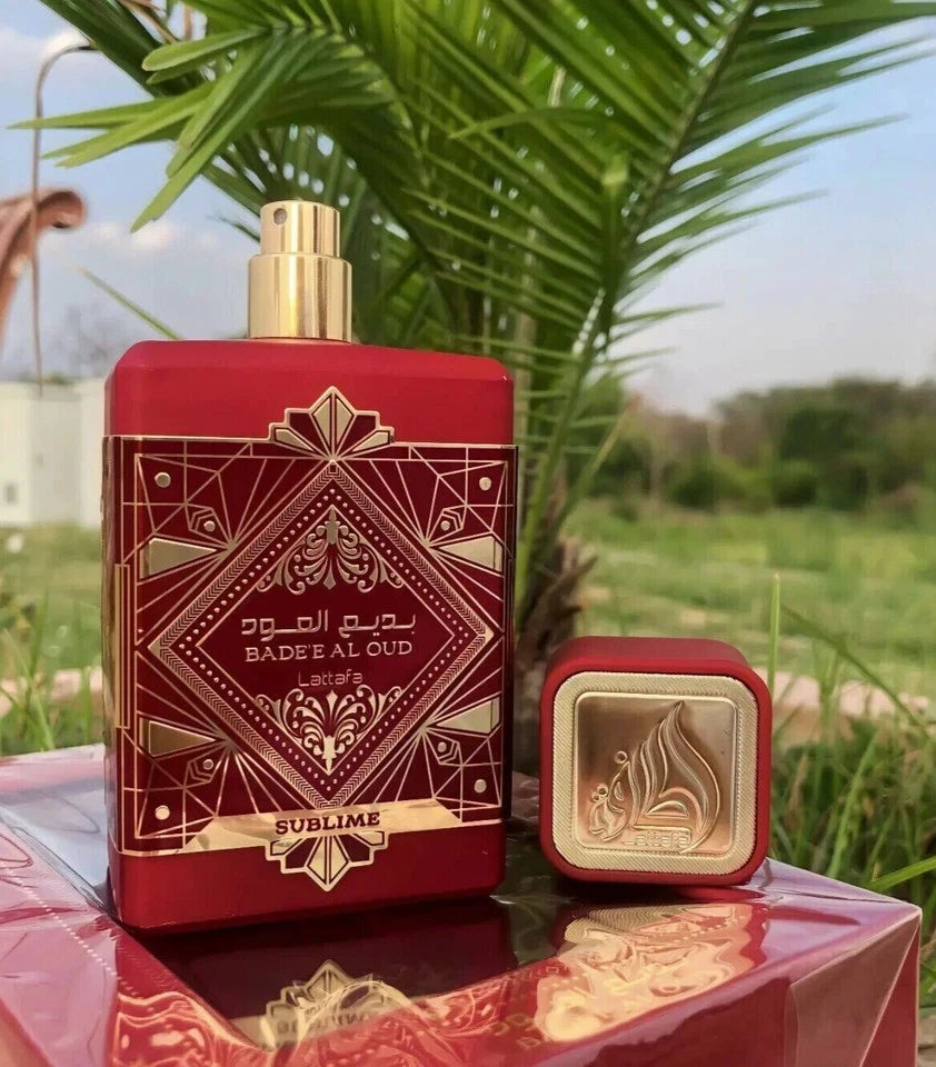 Red and gold perfume bottle with decorative design on a reflective surface with greenery in the background