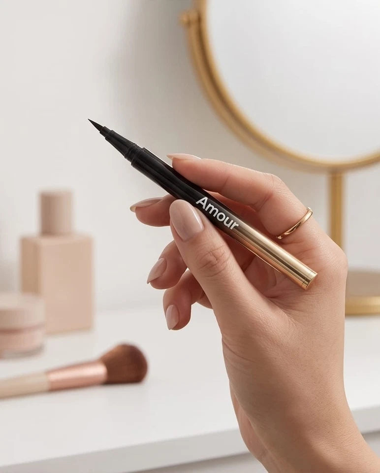 Hand holding a makeup pen labeled 'Amour' with cosmetic items in the background
