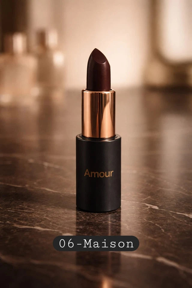Lipstick with gold cap and black casing on a reflective surface, labeled 'Amour 06-Maison'.