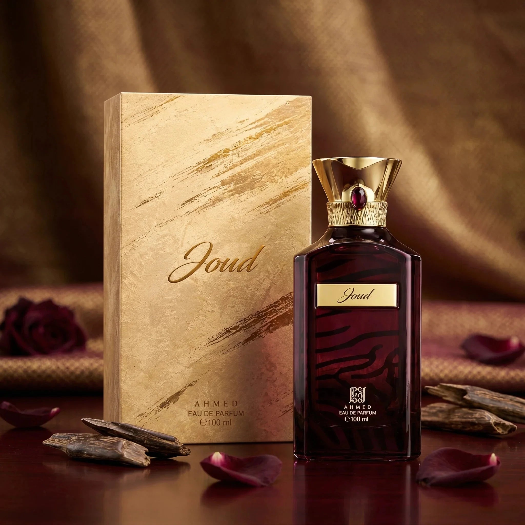 Joud perfume bottle and packaging on a wooden surface with rose petals and stones.